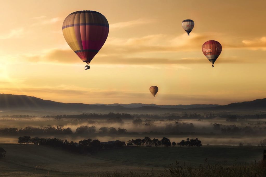 Hot air balloons floating over misty fields at sunrise, creating a picturesque adventure scene.