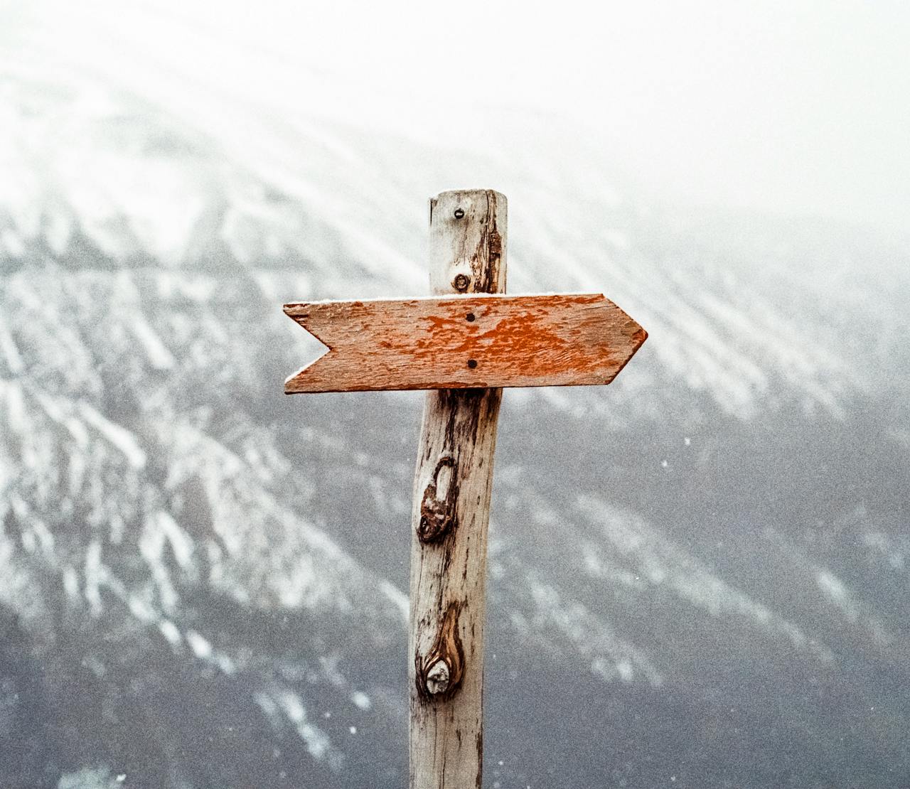 gallery-02 A wooden arrow signpost points the way amidst a snowy mountain landscape.