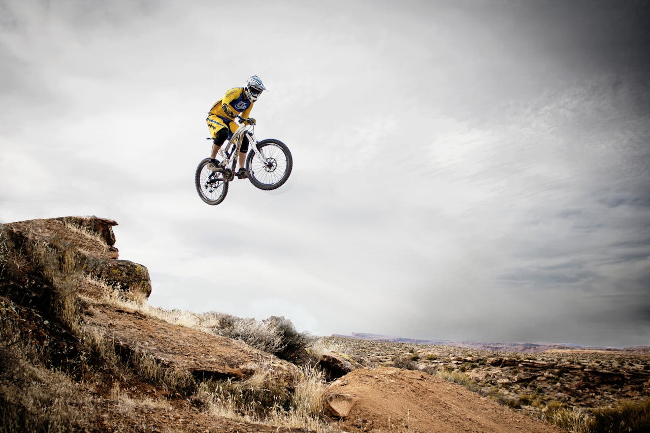 services-img A cyclist performs a daring jump off a rocky cliff under a cloudy sky.